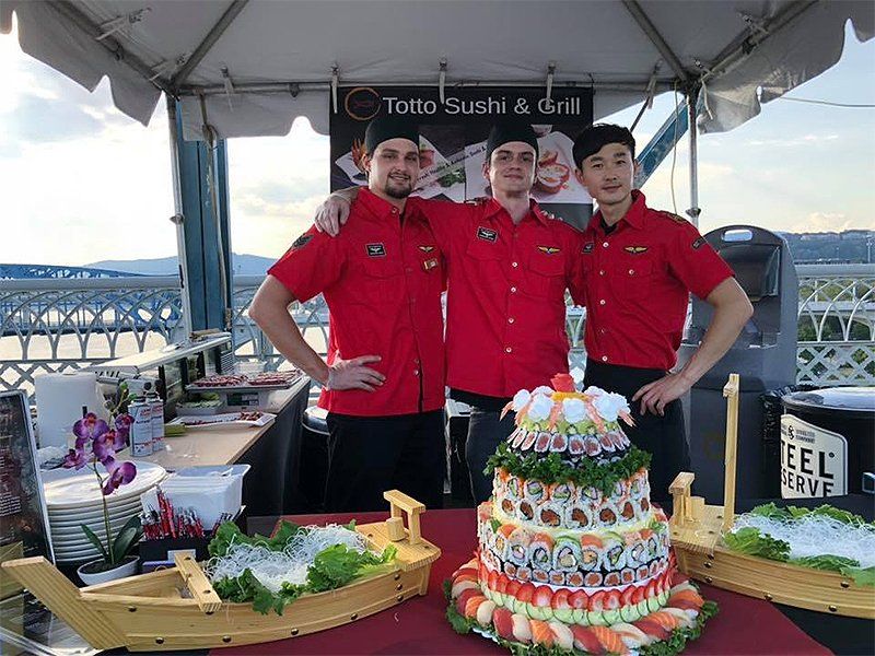 Three men are standing in front of a table with a cake on it.