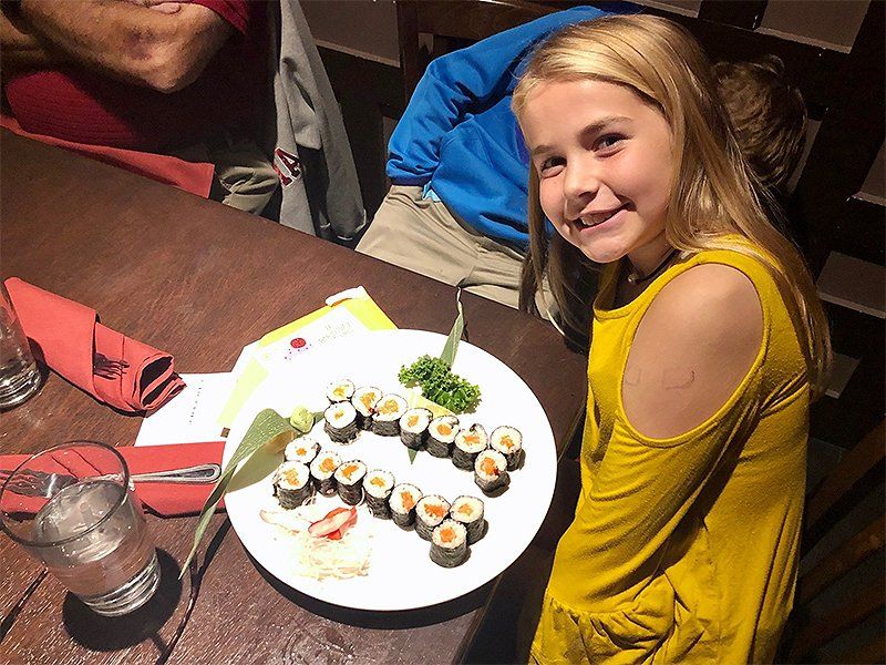 A little girl is sitting at a table with a plate of sushi on it