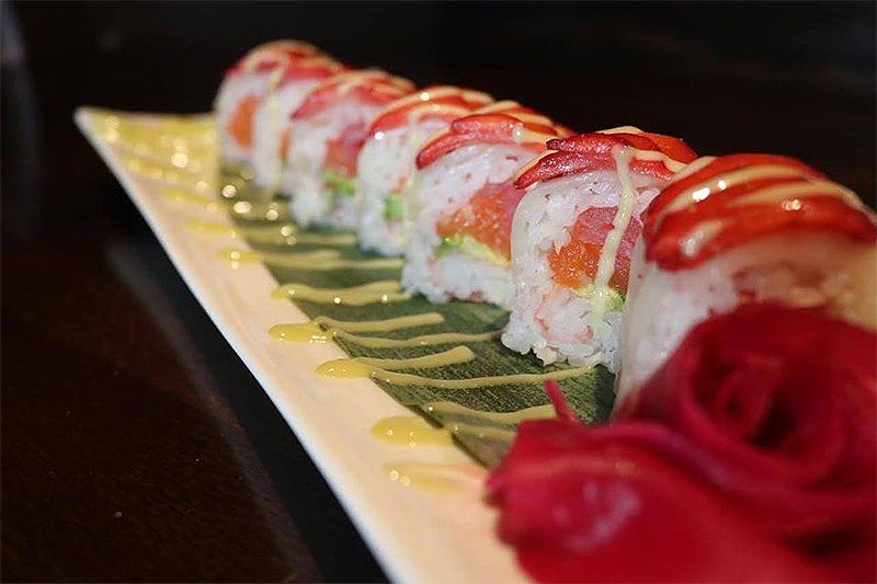 A row of sushi rolls on a white plate with a red rose in the background.