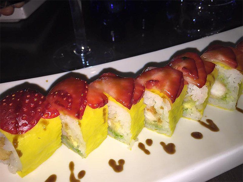 A row of sushi rolls with strawberries on top on a white plate