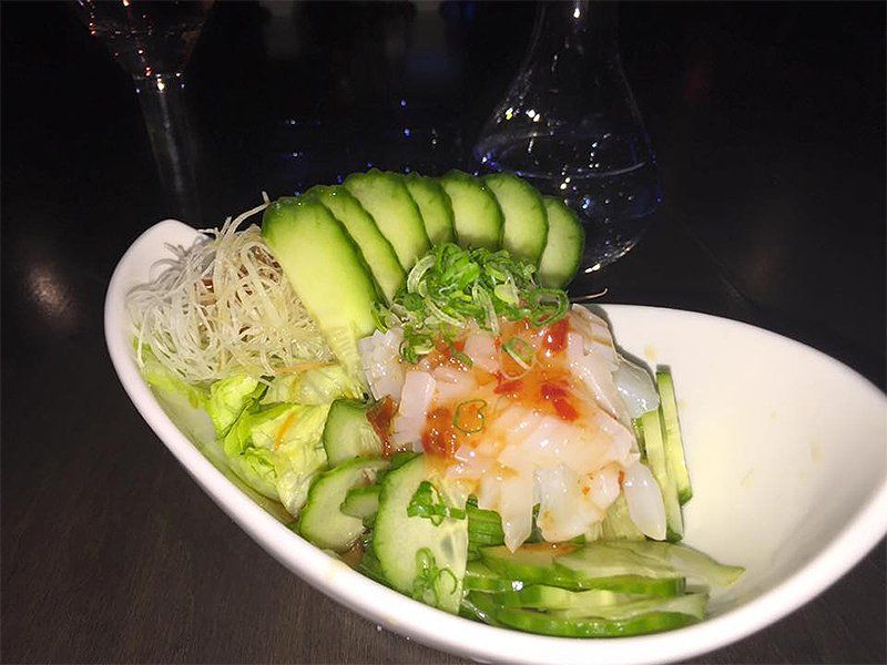 A white bowl filled with sliced cucumbers and shrimp.