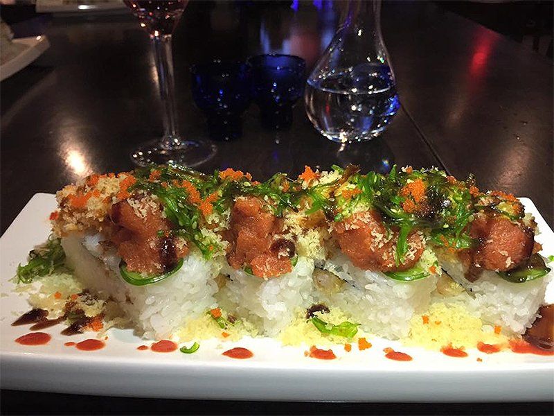 A plate of sushi with a glass of wine in the background