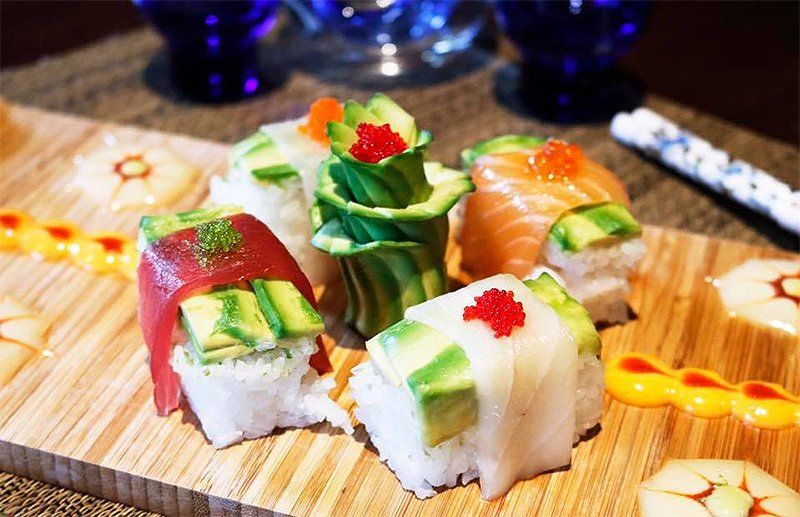 A wooden cutting board topped with sushi and avocado rolls