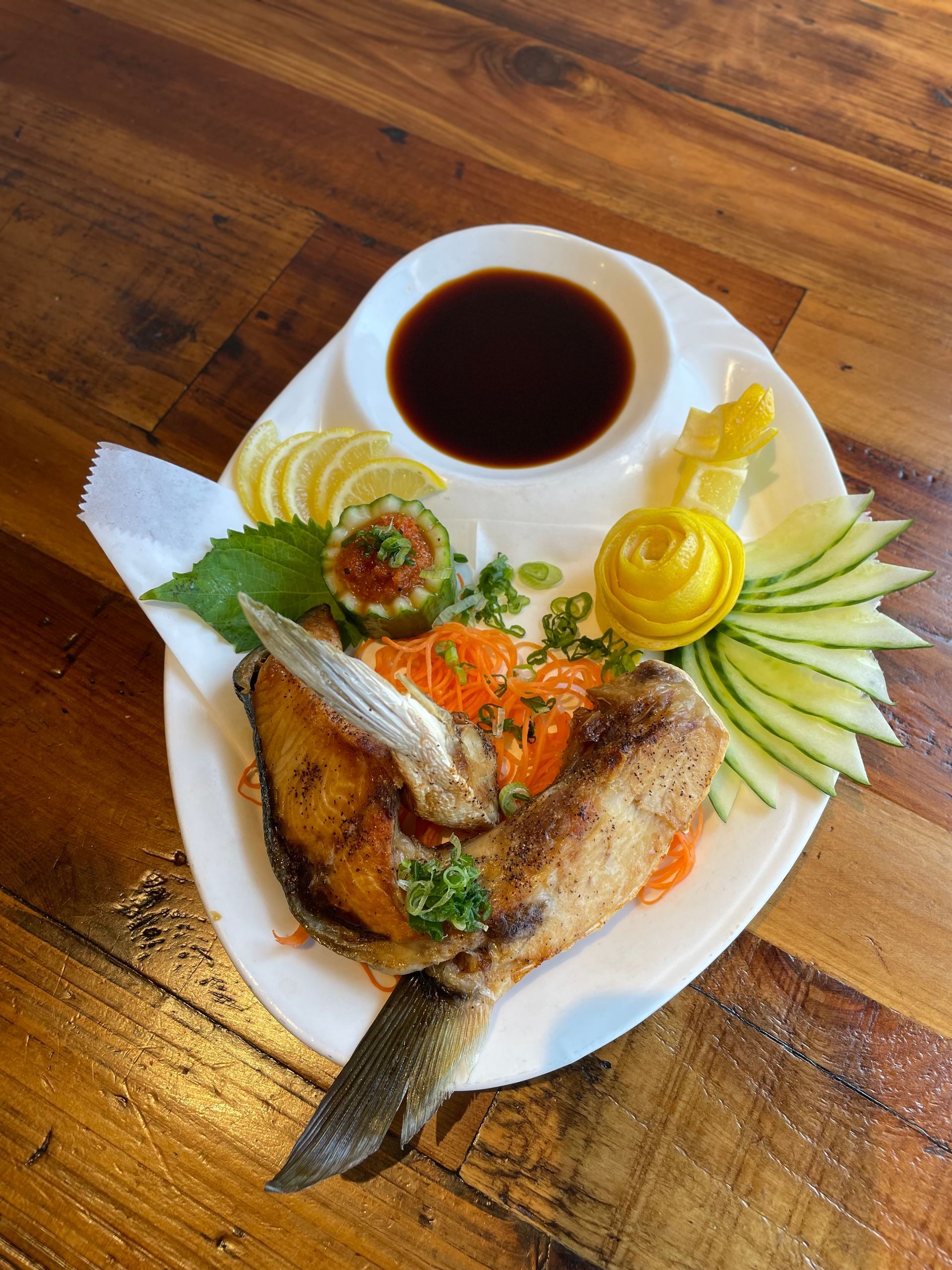 A plate of food with a fish and vegetables on a wooden table.
