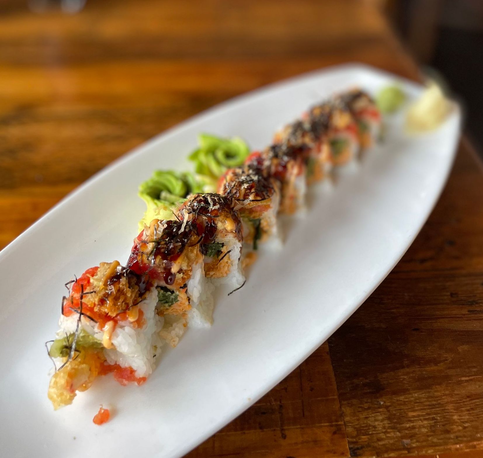 A close up of a sushi roll on a white plate on a wooden table.