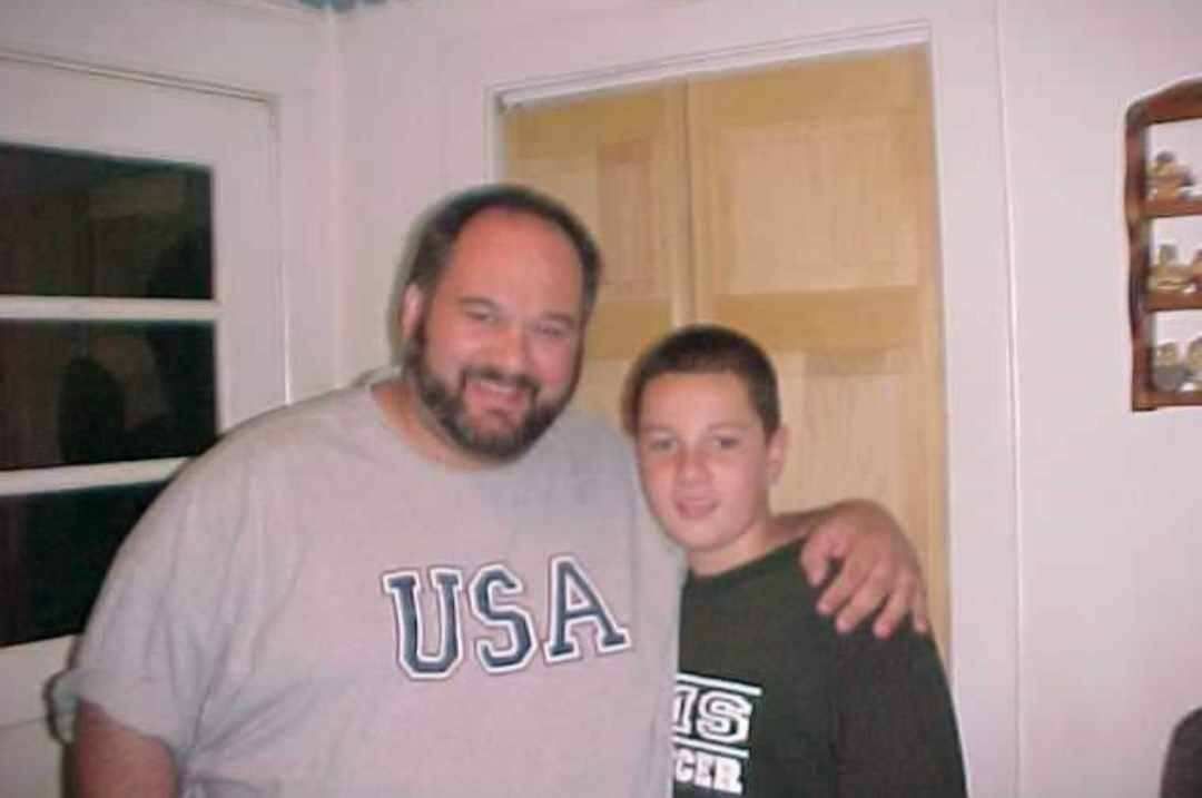 A man wearing a usa shirt stands next to a young boy