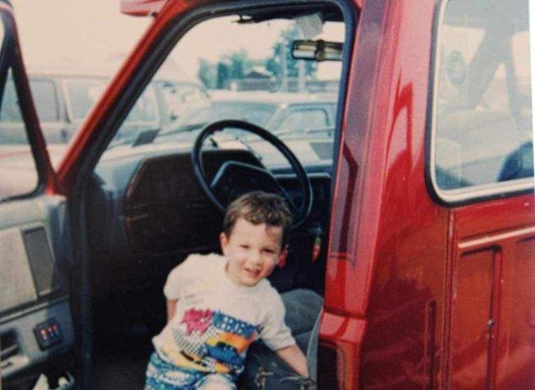 A young boy is sitting in the driver 's seat of a red truck