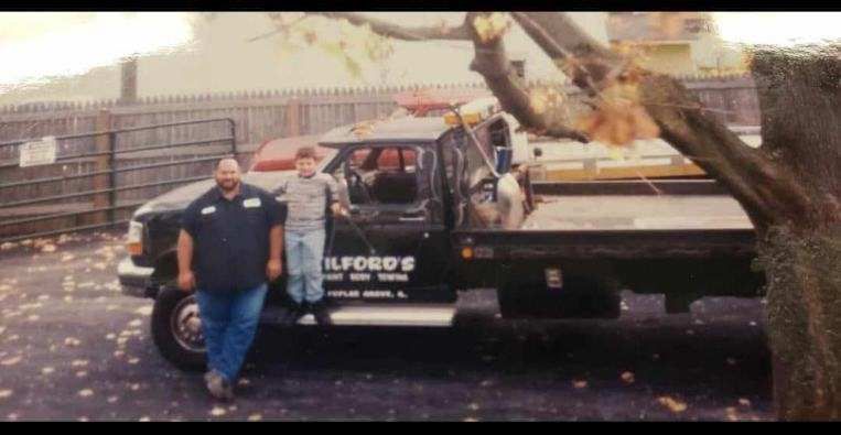 Two men are standing in front of a tow truck.