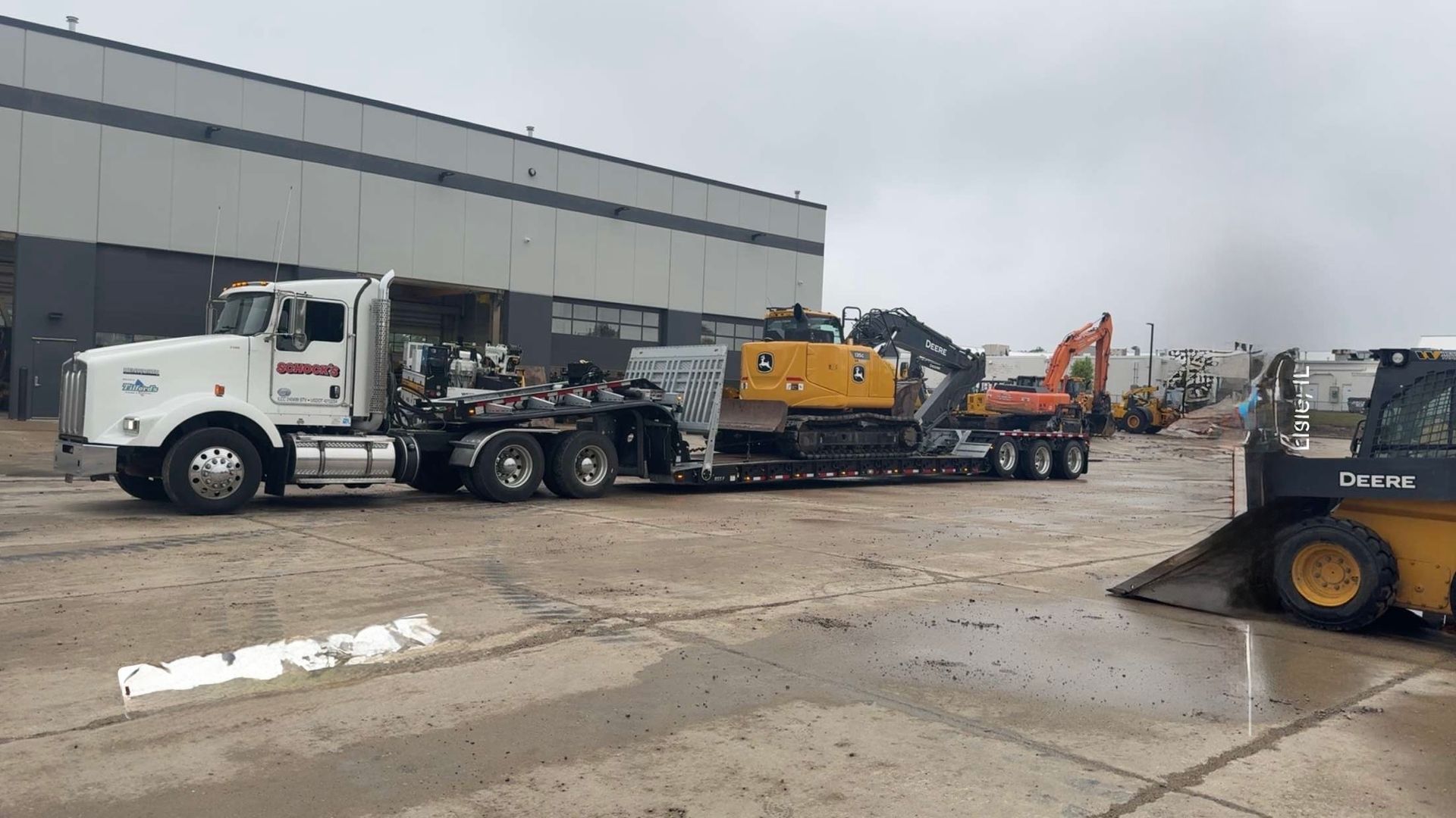 A semi truck is carrying a yellow excavator on a trailer.