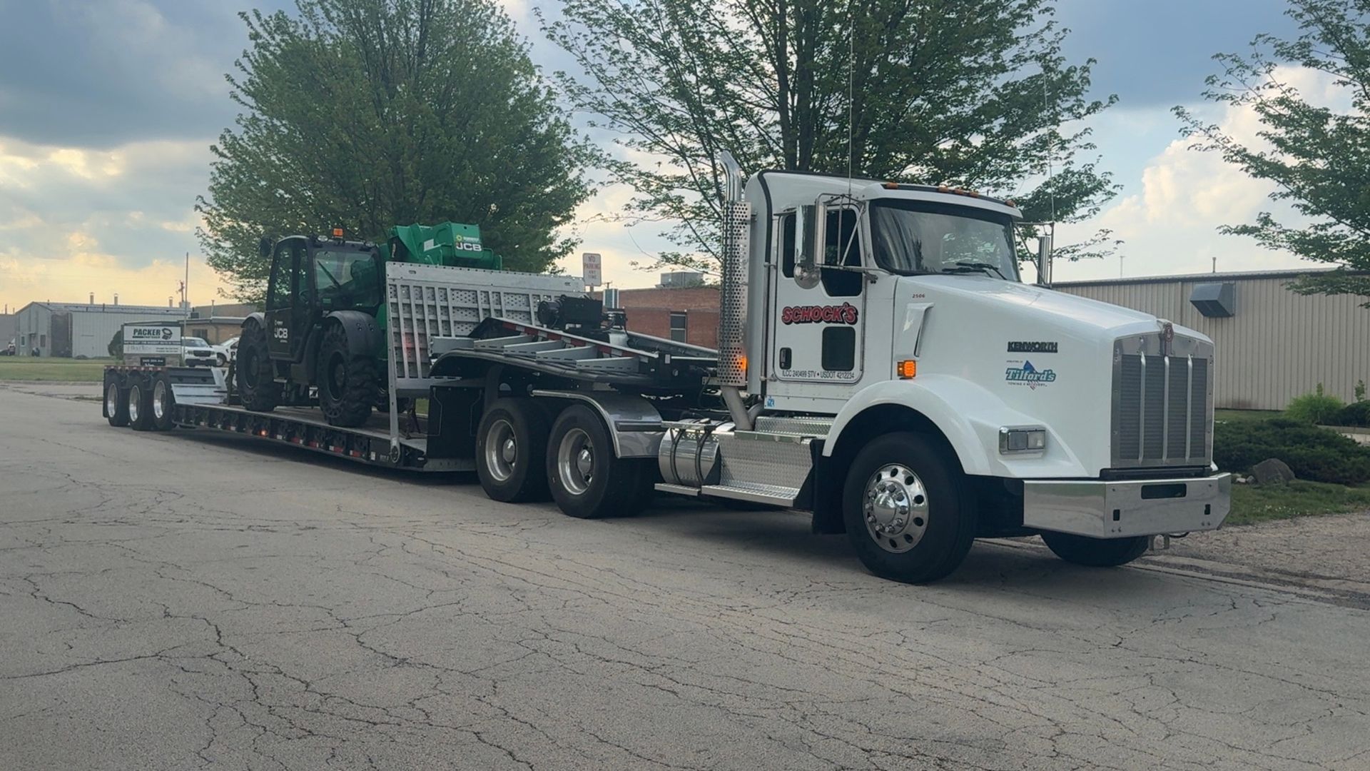 A white semi truck is carrying a trailer with a tractor on it.
