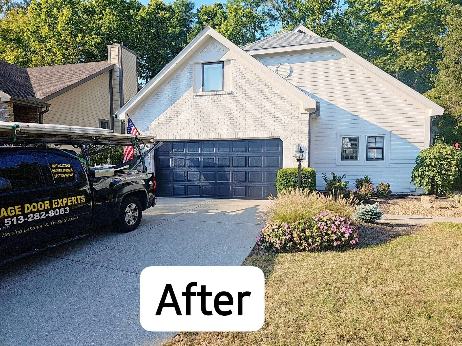 After view of a beige house with a dark garage door and landscaping, with a work van in the driveway.
