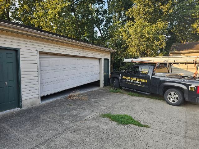 Black truck parked in a driveway beside a white garage door and house siding.