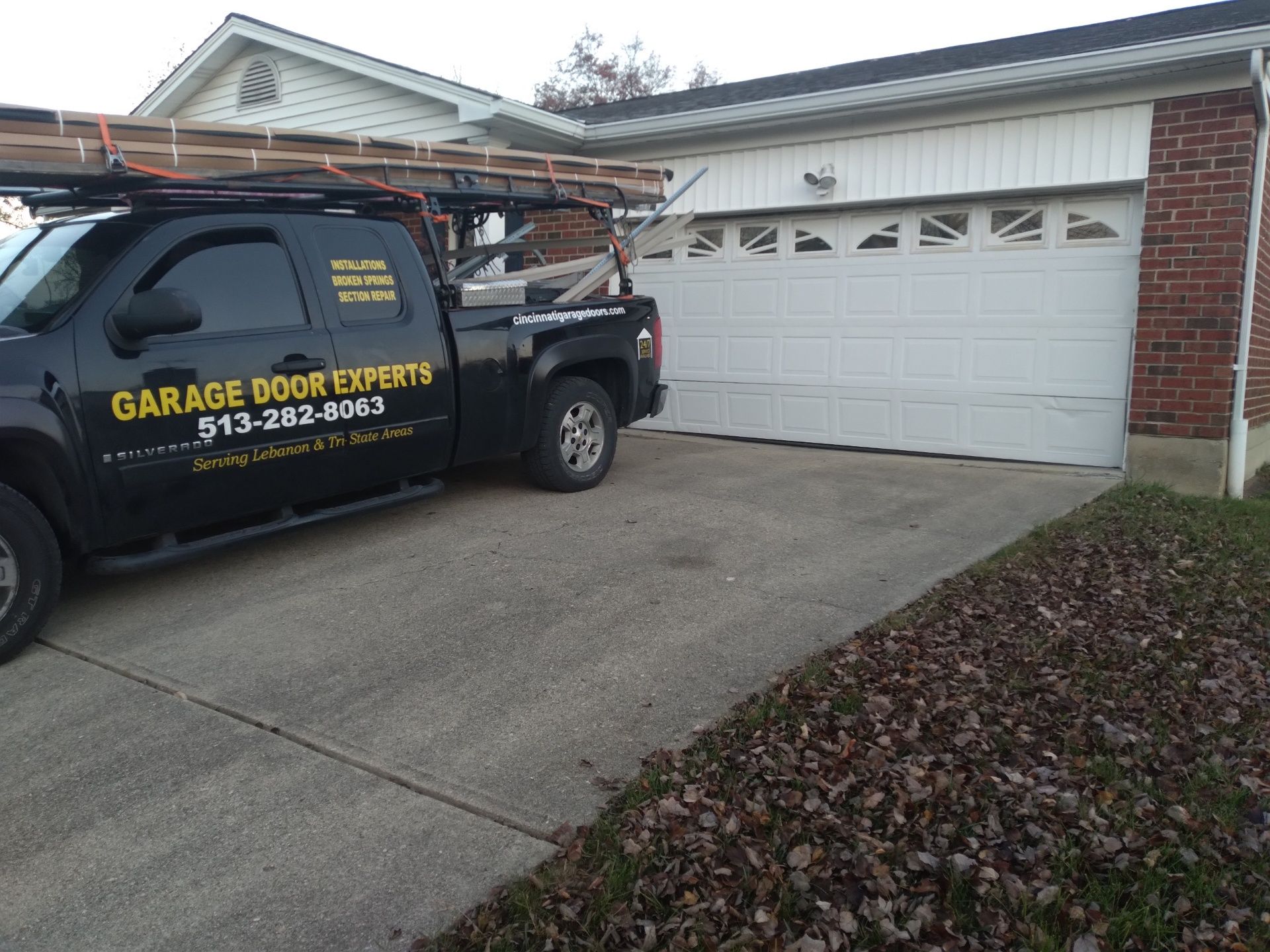 Garage door repair van parked in a driveway beside a white garage door and brick house.