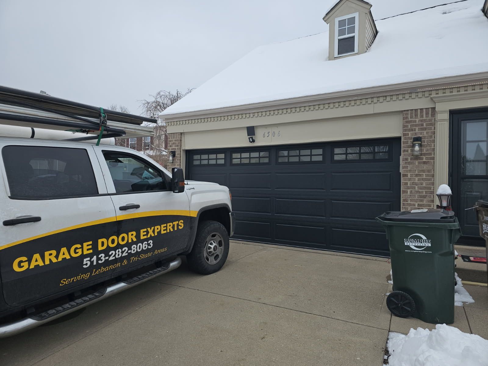 Garage Door Experts service van parked beside a snow-covered residential garage.