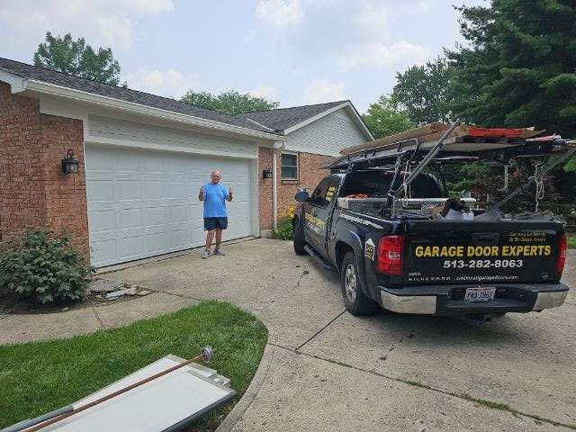 Worker by a garage door service truck beside a brick house, with a man standing near the garage