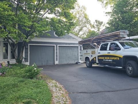 White utility truck parked in driveway beside a gray two-car garage and trees.