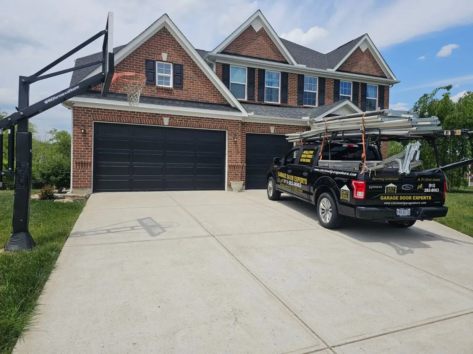 Two-story brick house with black garage, concrete driveway, and a black pickup truck parked out front