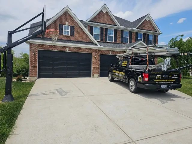 Brick two-story house with black garage, concrete driveway, and a black pickup truck parked out front.