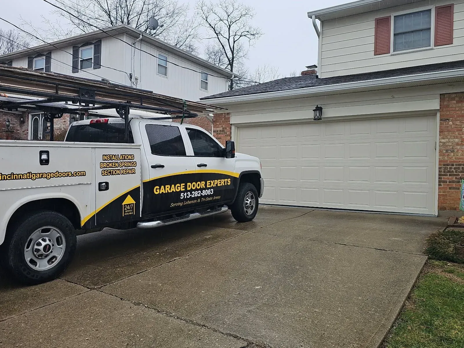Tow truck parked in a driveway beside a garage and house on a cloudy day