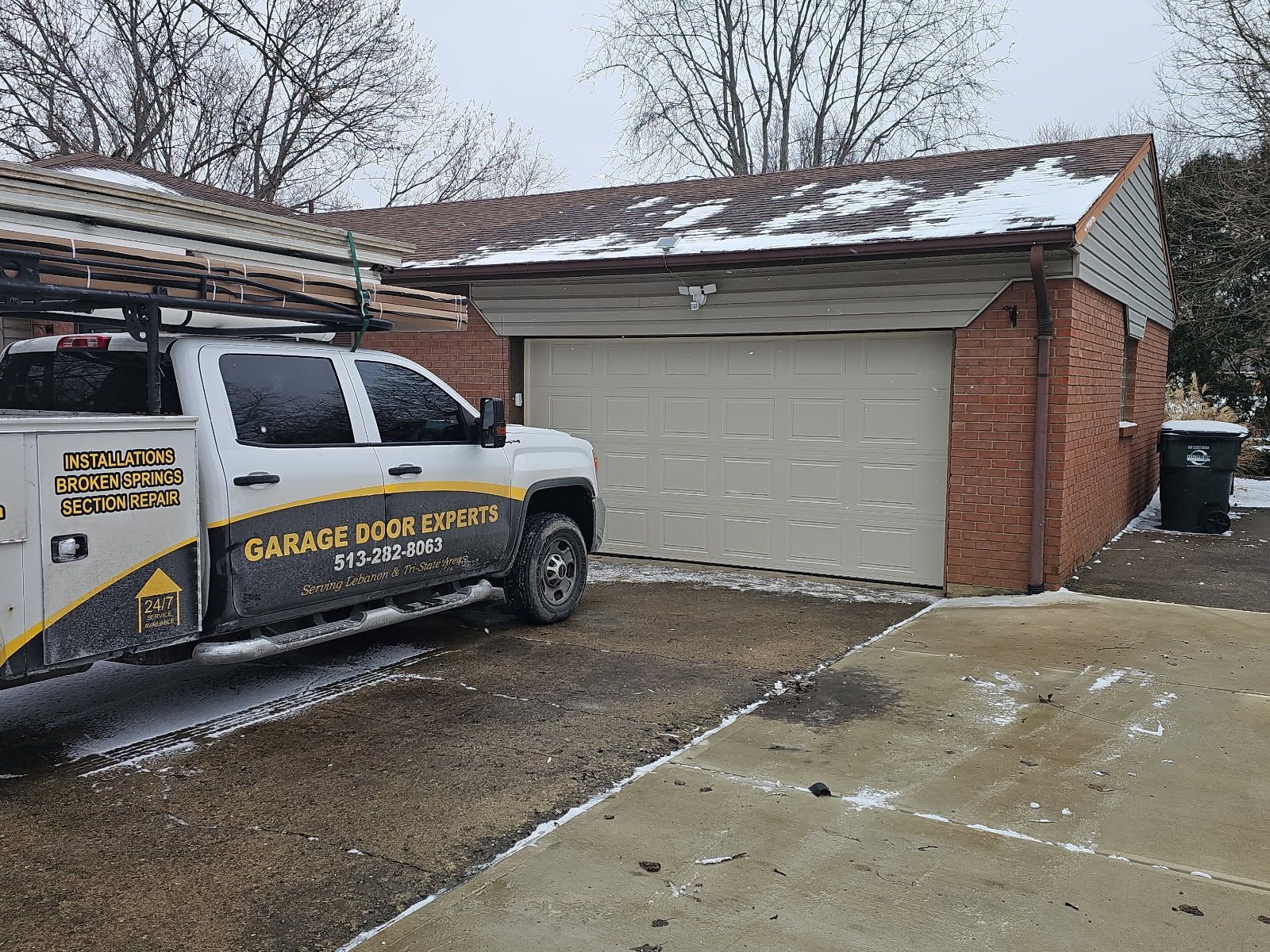 Garage door repair truck parked beside a brick house with a snow-dusted driveway