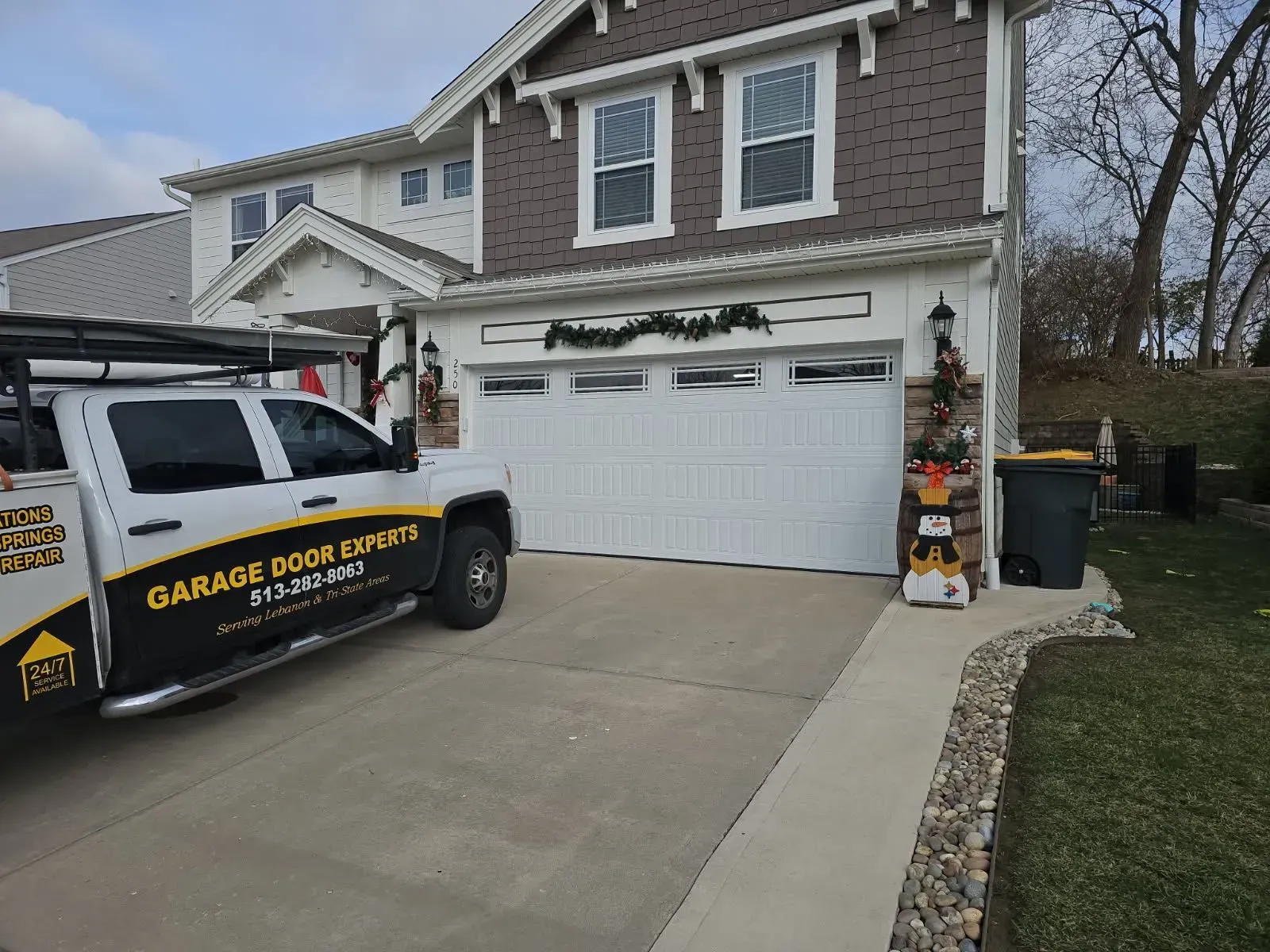 Garage door service truck parked in a suburban driveway beside a two-story house.