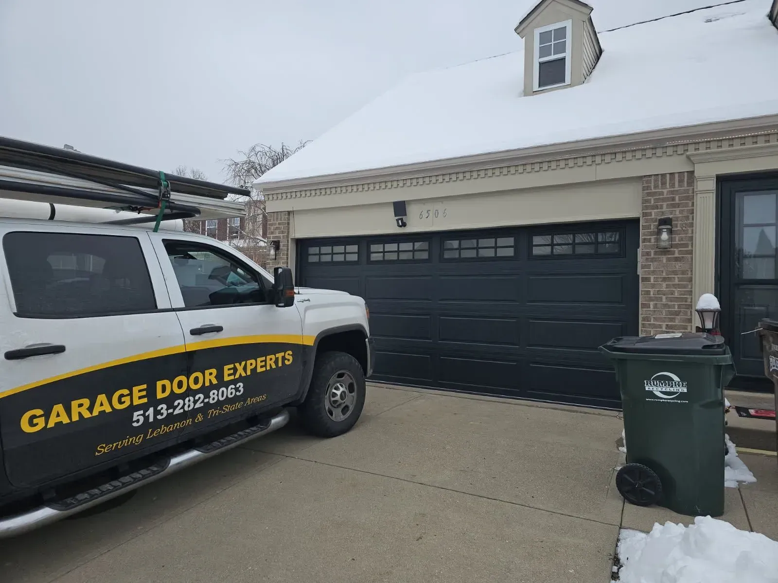 Garage Door Expert service truck parked in a snowy driveway beside a black garage door.