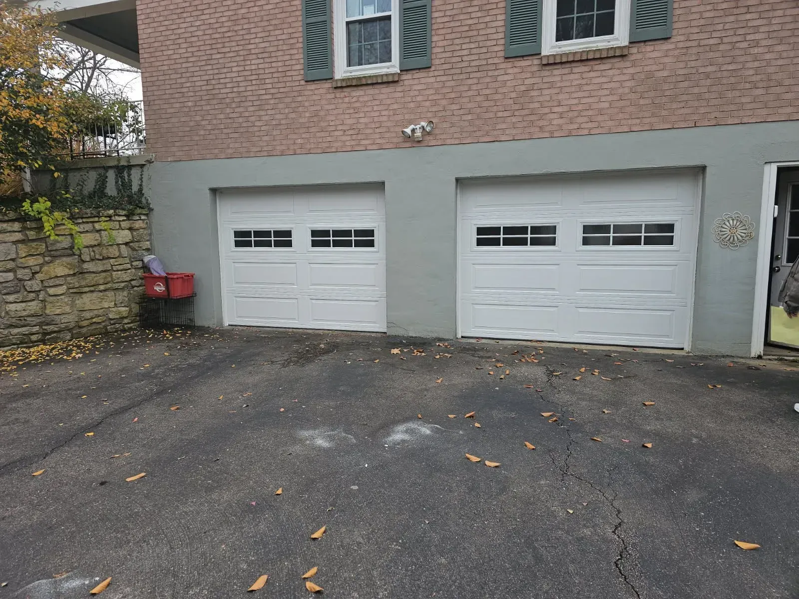 Two white garage doors under a brick house, with a dark driveway in front.