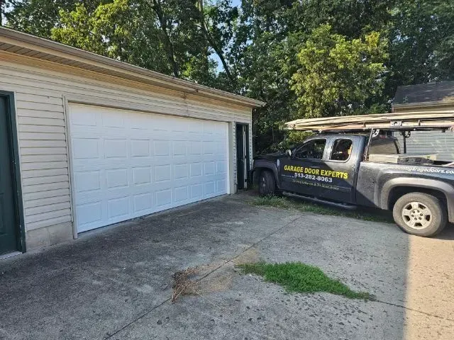 Garage with white door beside a parked dark SUV and work truck in a driveway.