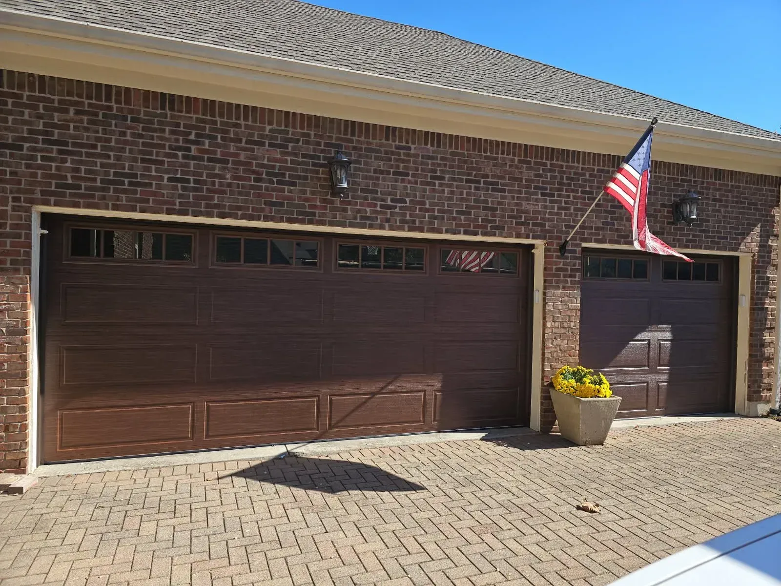 Brick house exterior with two brown garage doors, a U.S. flag, and a flower pot by the entry