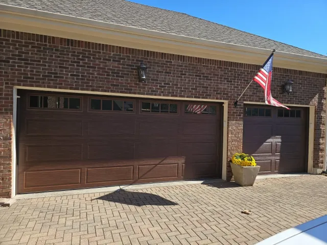 Brick house with two brown garage doors, a U.S. flag, and a potted yellow flower on the driveway.