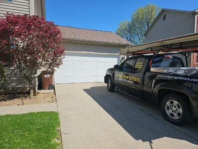 Black service truck parked in a driveway beside a white garage under a sunny blue sky.