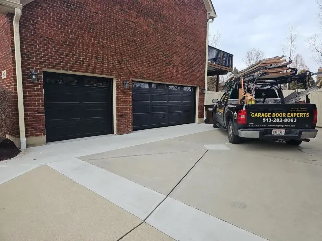 Two black garage doors on a brick building beside a work truck on a concrete driveway.