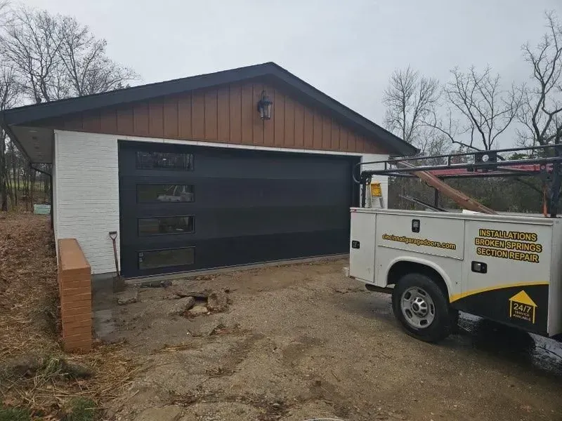 Utility trailer parked beside a dark garage under construction on a muddy driveway.