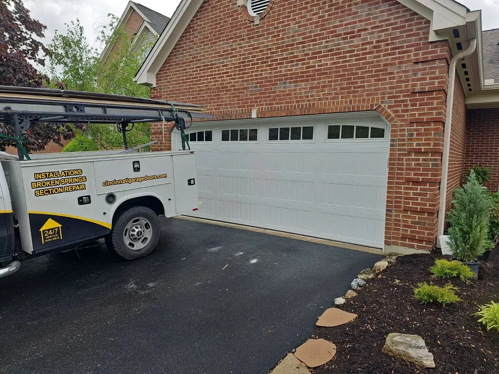 Worker in a utility truck parked in front of a brick house and white garage door
