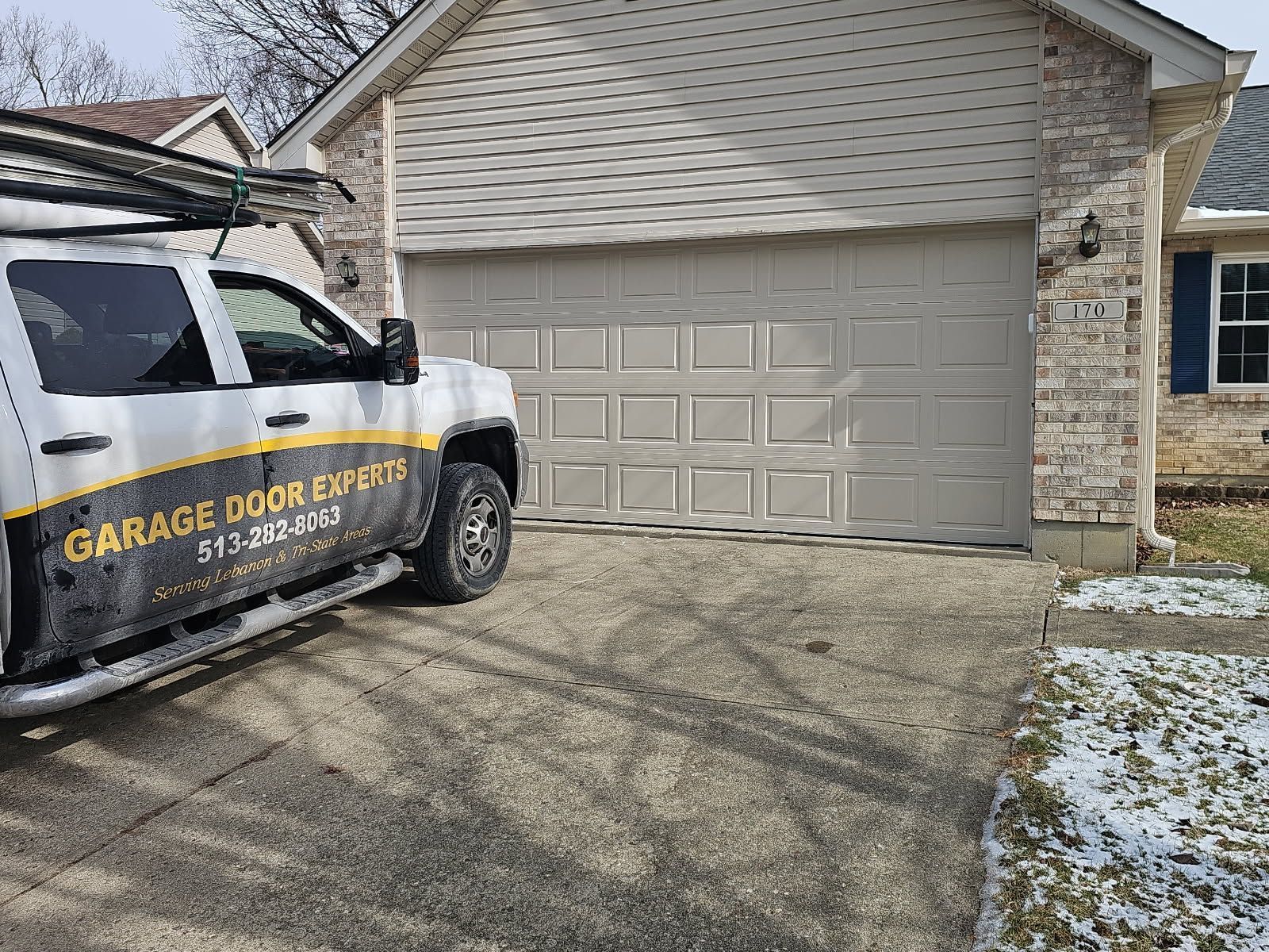 Service van parked in a driveway in front of a beige garage door, with light snow on the ground.