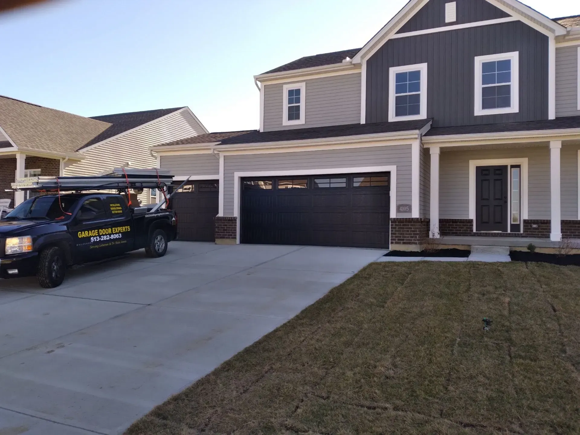 New suburban house with gray siding, two-car garage, and a black service truck in the driveway