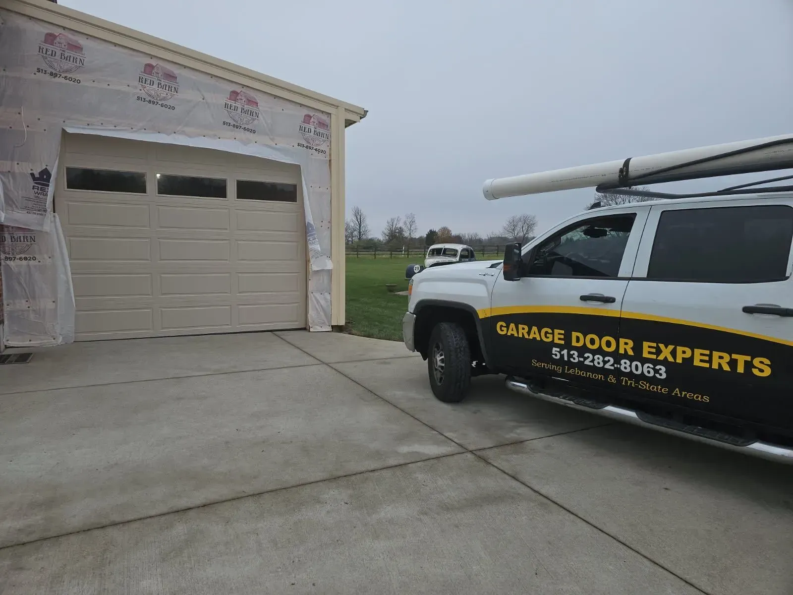 Garage Door Experts truck parked beside a garage with a tan overhead door on a cloudy day