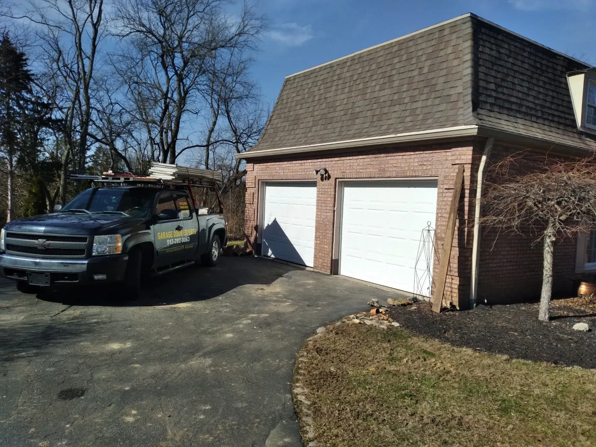 Truck parked beside a brick garage with white doors on a sunny driveway
