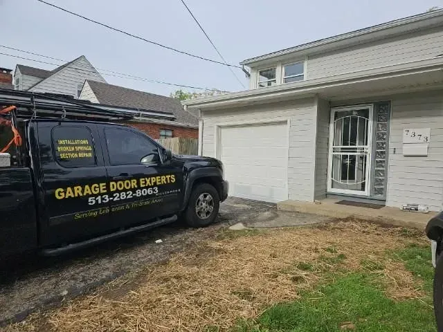 Black garage door service truck parked beside a house with a white garage door and porch