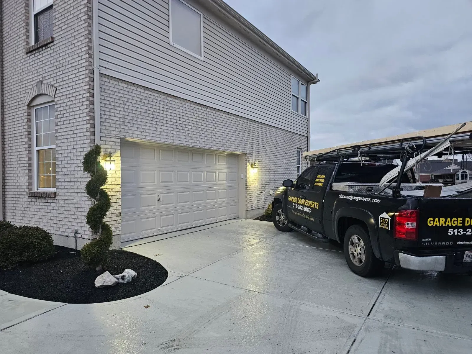 Driveway beside a two-story house with a garage and a black service truck parked outside at dusk