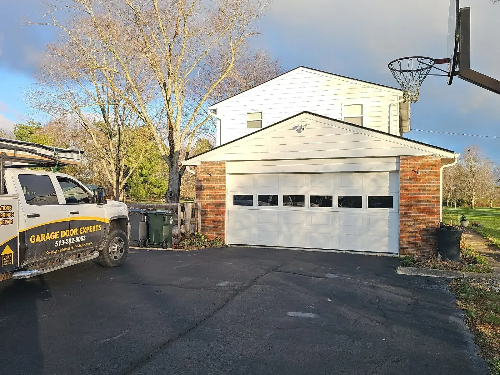 Suburban driveway with a white garage, blacktop paving, trees, and a utility truck on the left