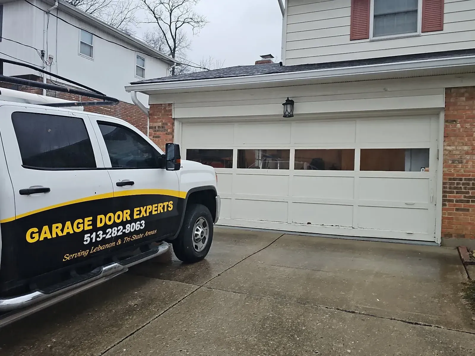 Garage door repair van parked in front of a white house with a damaged garage door