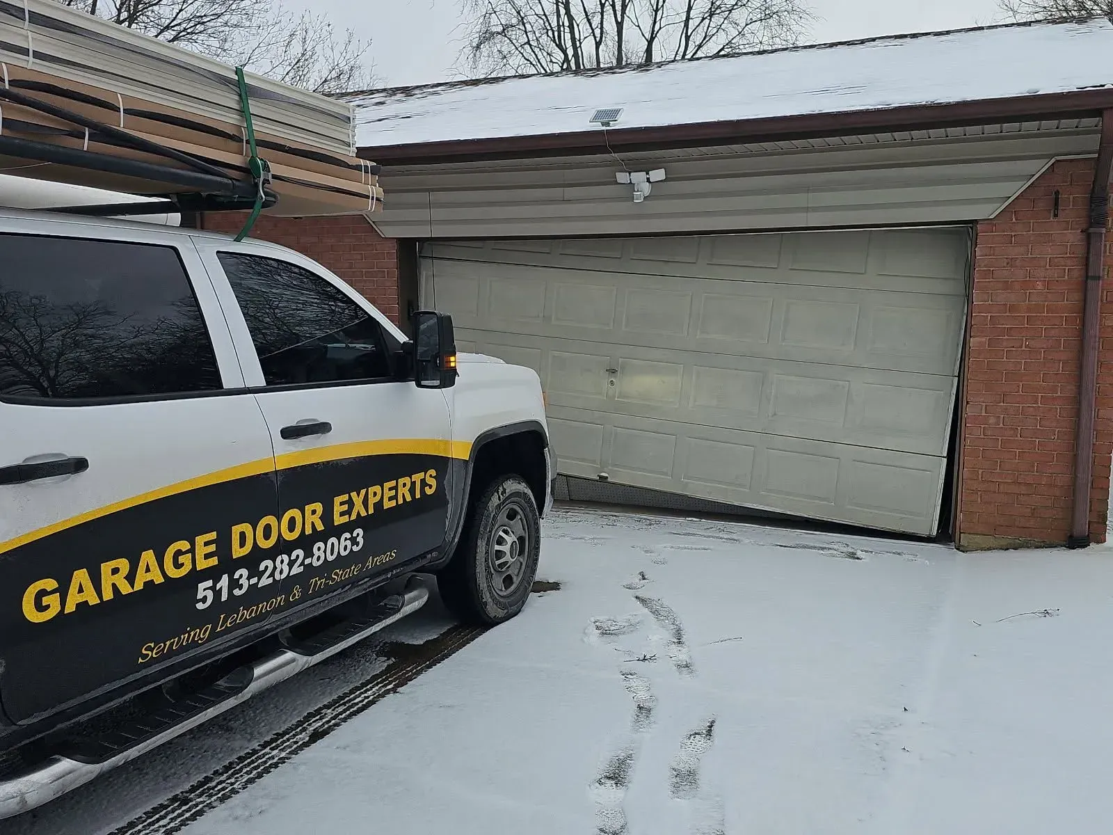 Snowy driveway with a garage door repair truck parked beside a closed white garage door.