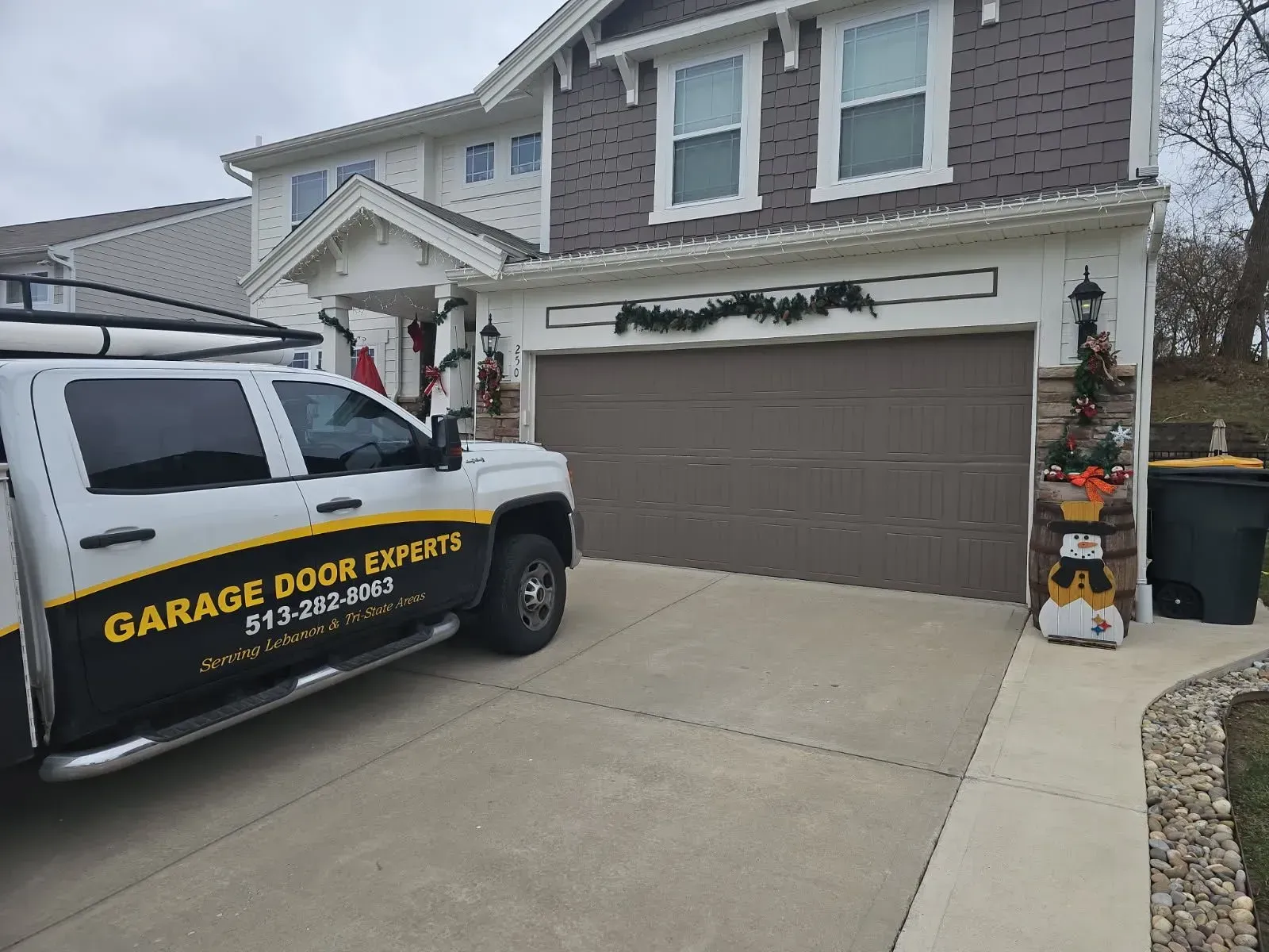 Garage door repair truck parked in front of a two-story suburban house with a brown garage door.