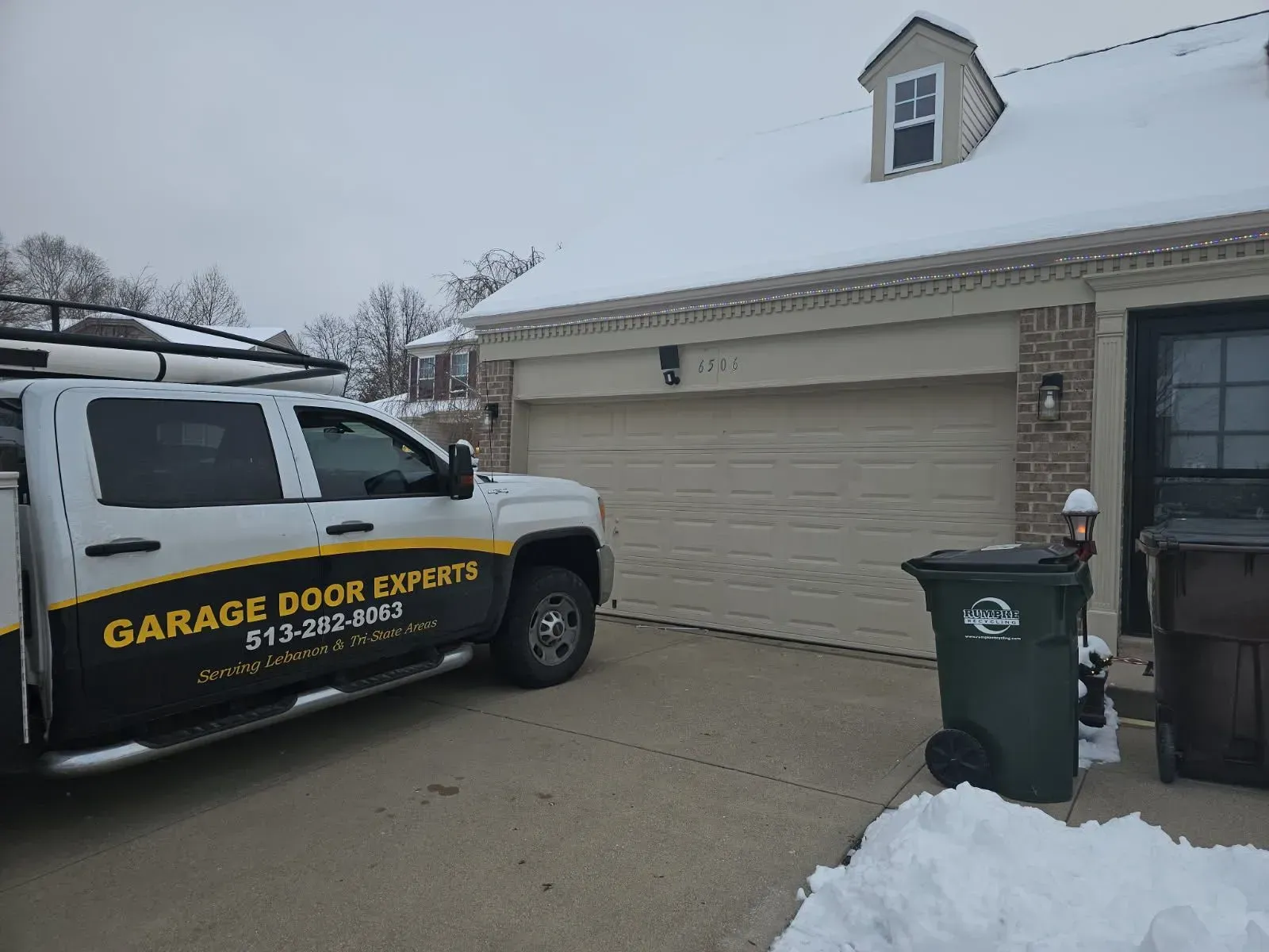 Garage door service van parked in a snowy driveway beside a tan garage.