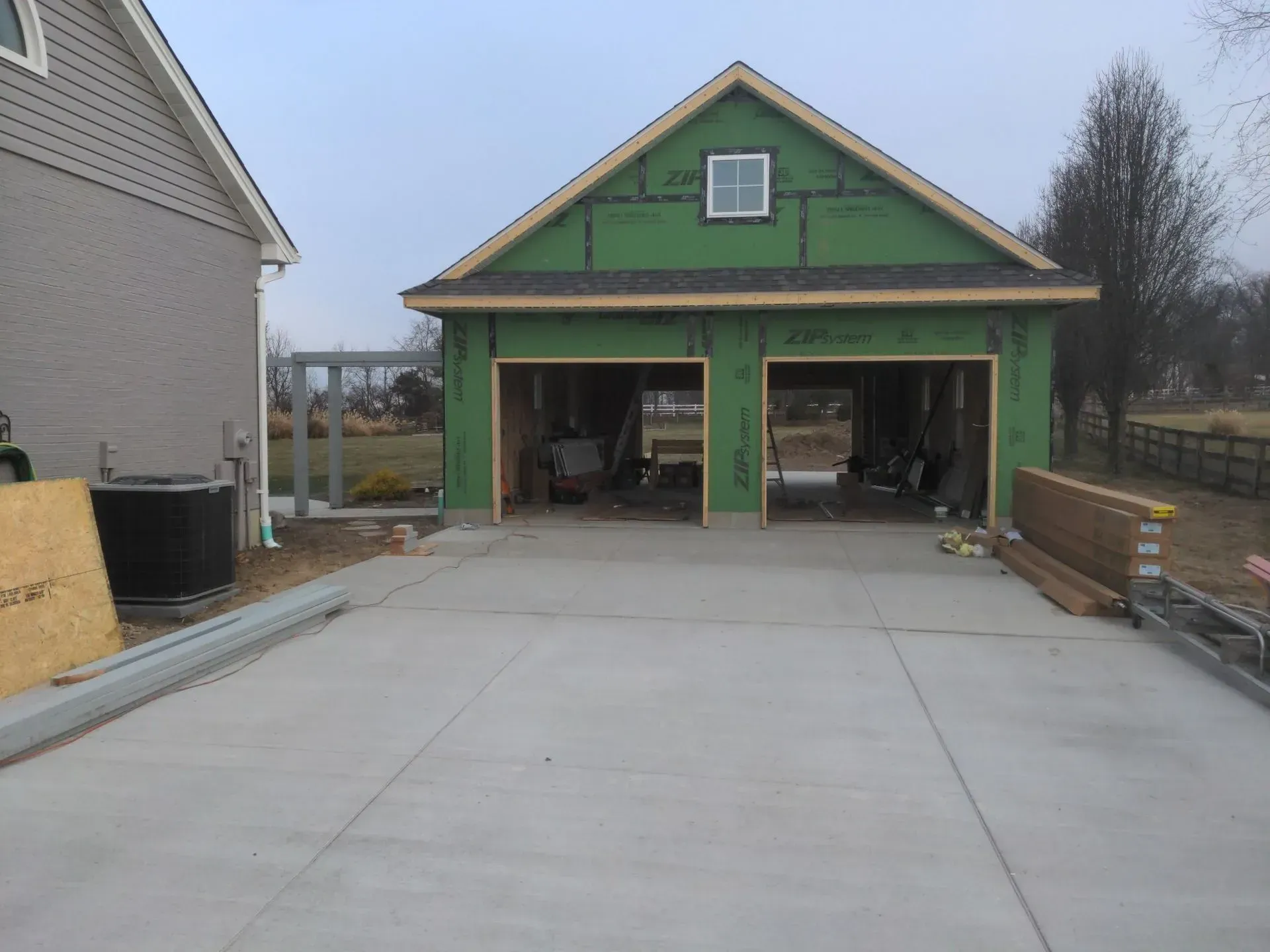Green garage under construction with open bays and a concrete driveway in front.