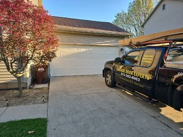 Black service truck parked in a suburban driveway beside a white garage and red-leaf tree