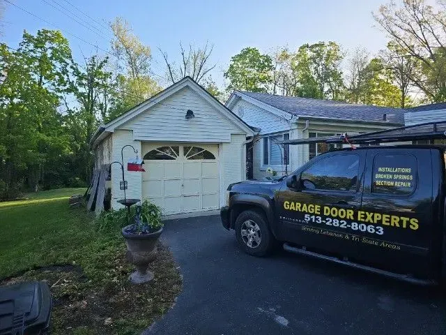 Garage door repair truck parked in front of a white garage in a suburban driveway.