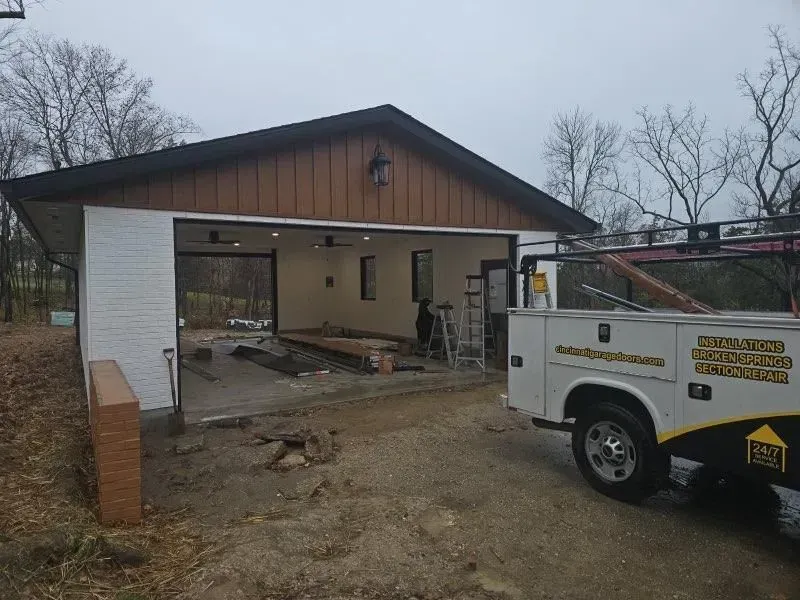Partially built garage with open front; utility truck parked beside it on a muddy lot.