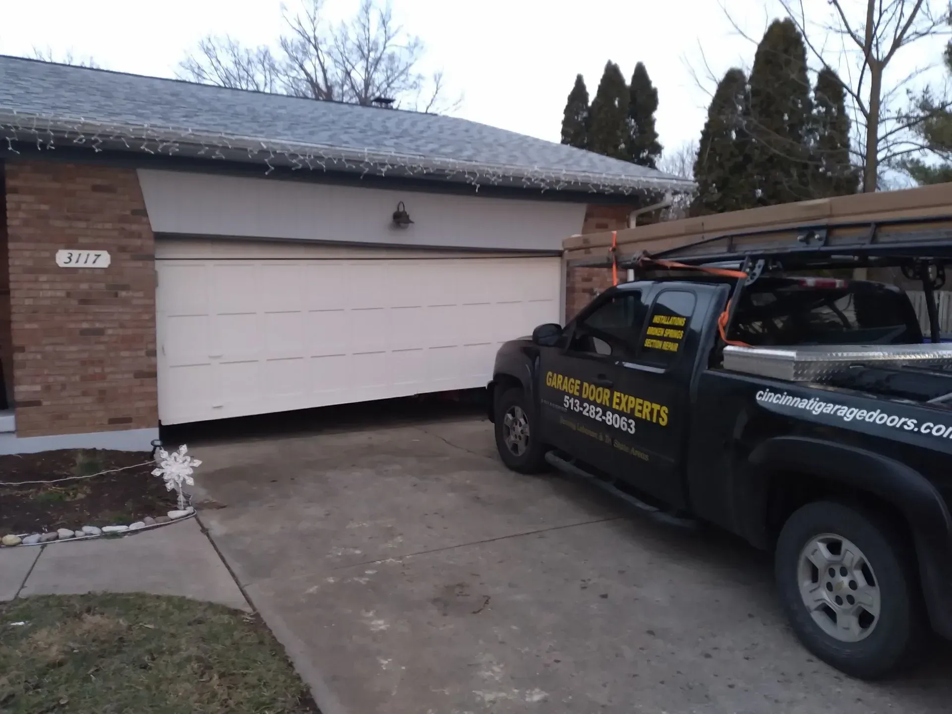 Black service truck parked in front of a beige garage door beside a brick house.